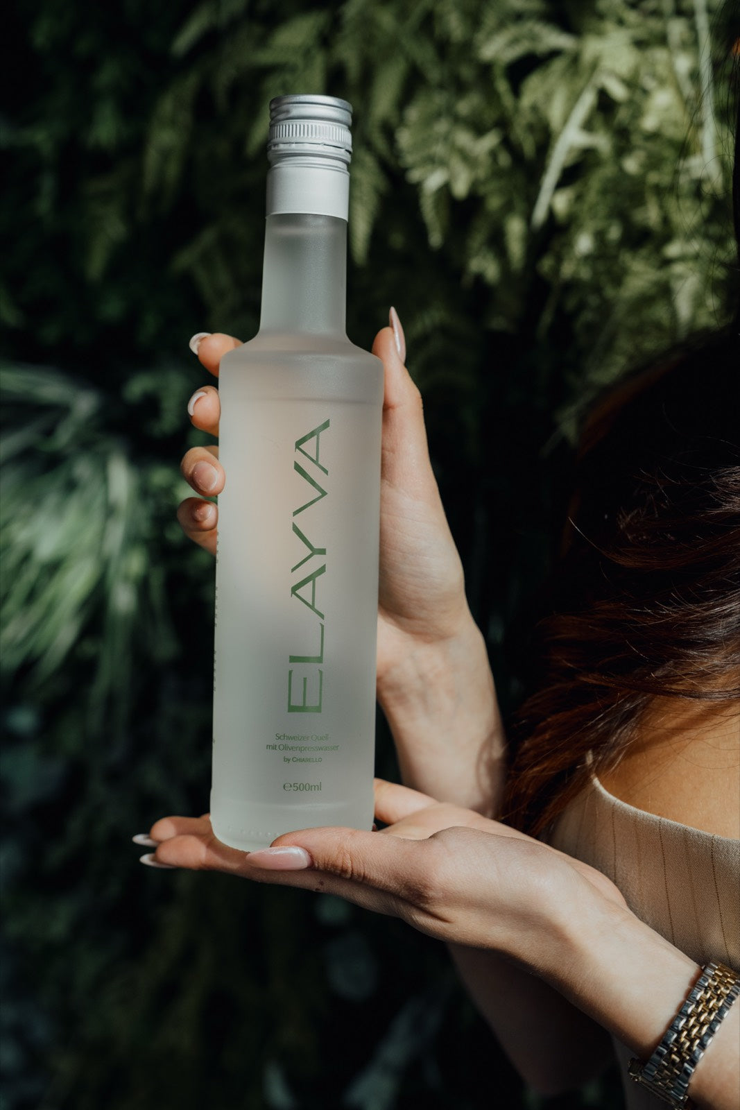 Hands holding an ELAYVA bottle among olive leaves