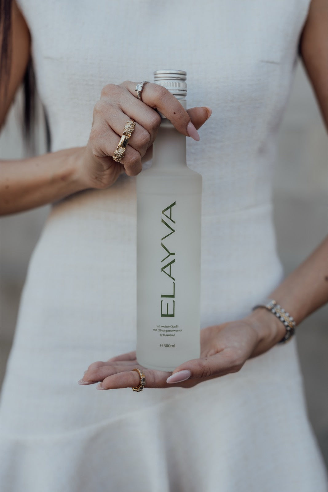 Woman in a white dress holding an ELAYVA bottle outdoors